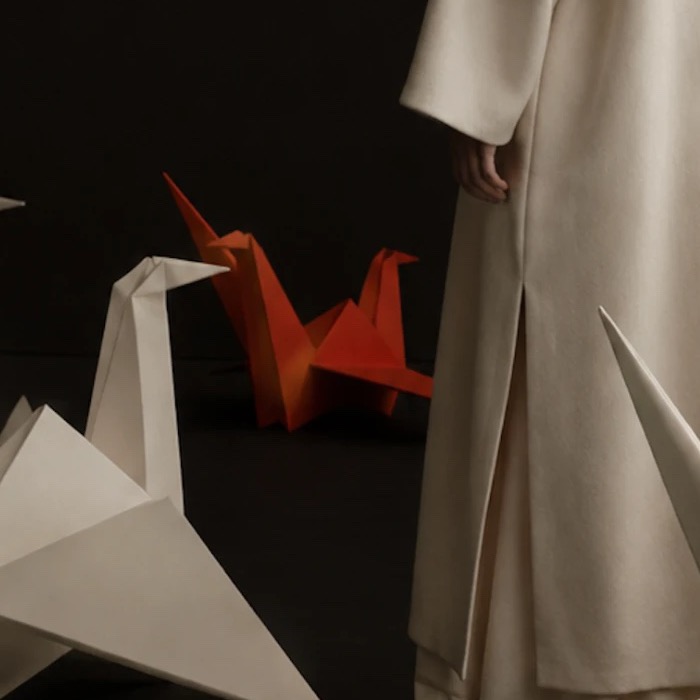 La grue d'origami cinabre près du manteau — une rouge parmi les blanches